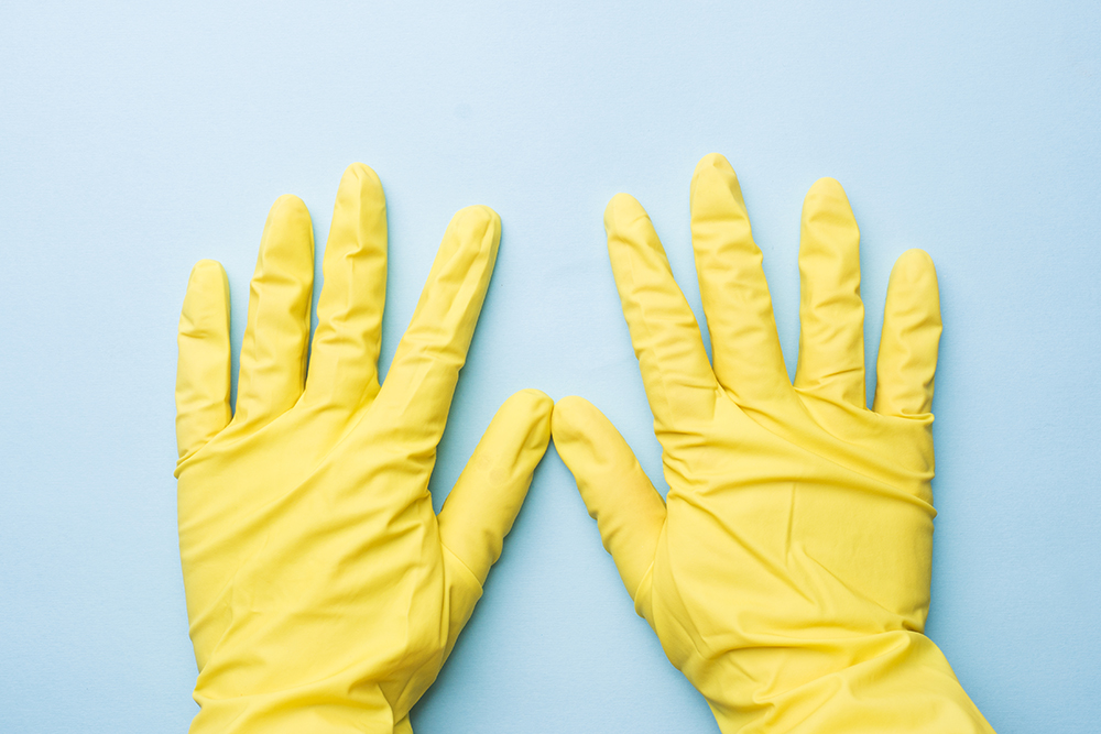 Hands in yellow gloves for cleaning on blue background. Home cleaning concept. Top view,