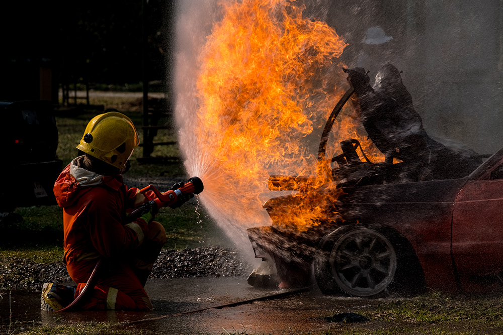 Firefighter is spraying water to extinguish the fire on a burning car.